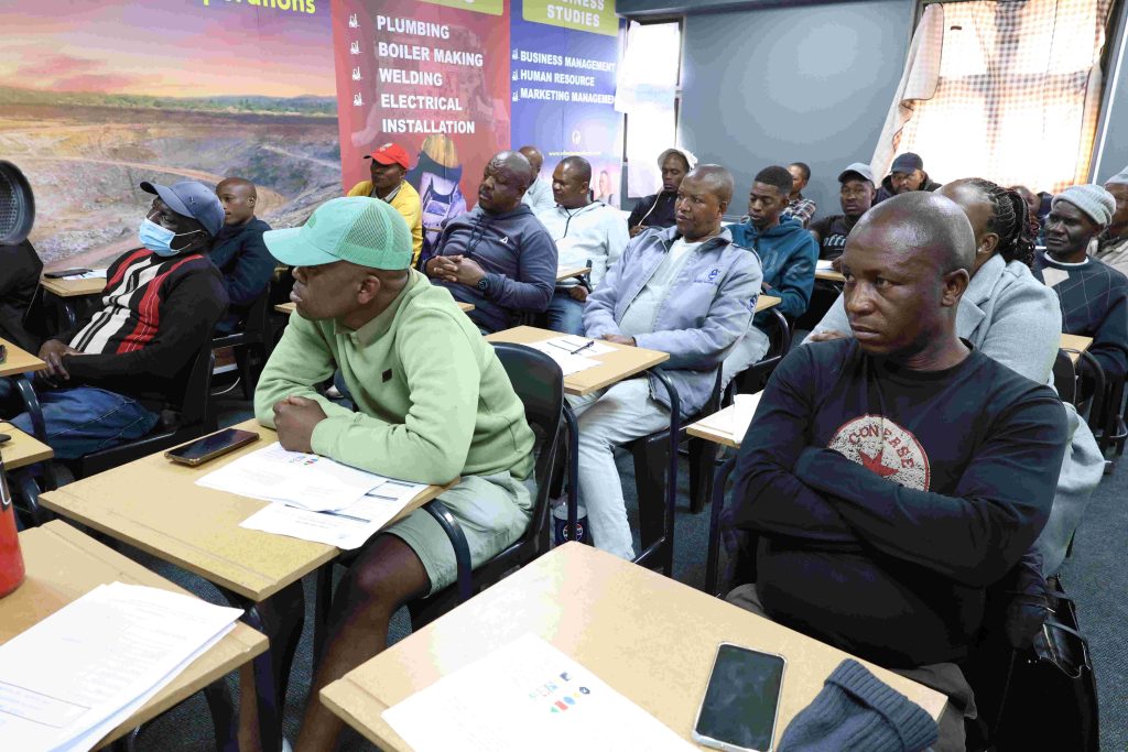 A full classroom of adult learners at Wheelset Academy, with a banner listing the trade and business programmes on offer